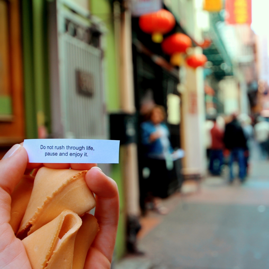 Pisces - fortune cookie writer - woman's hand holding a fortune cookie that's fortune reads "Do not rush through life, pause and enjoy it."