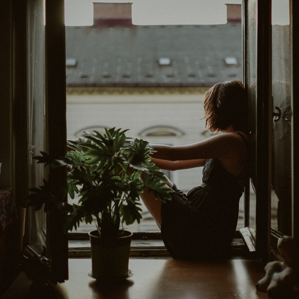 Pisces - your window alcove - woman sitting on window alcove seat in city with plant nearby