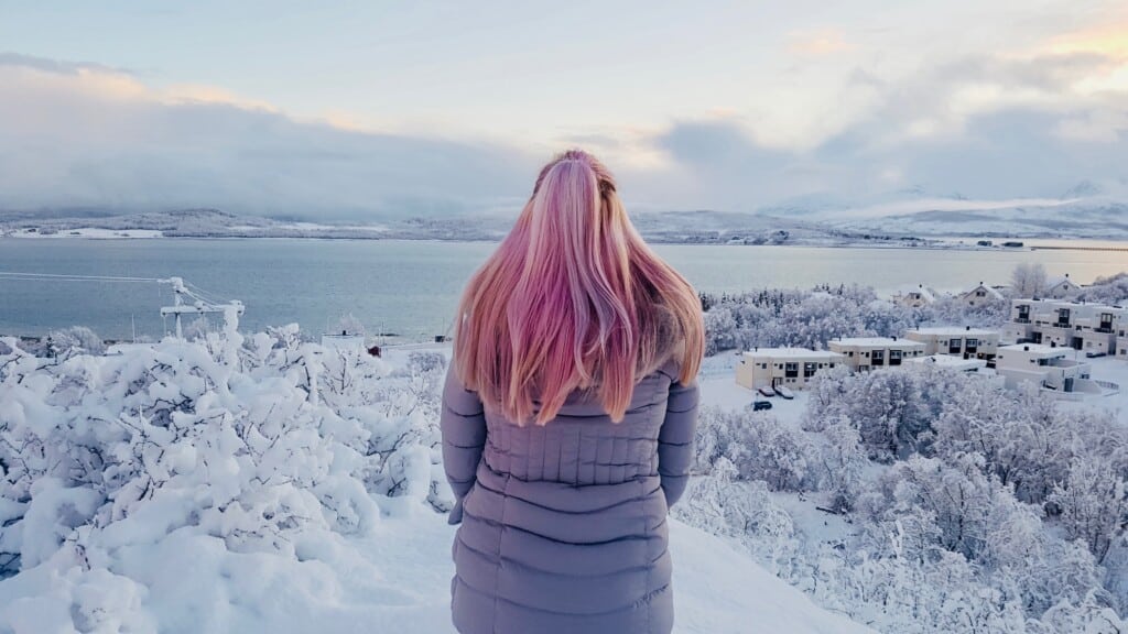 Woman with pink hair on top of hill looking out over snowy winter landscape