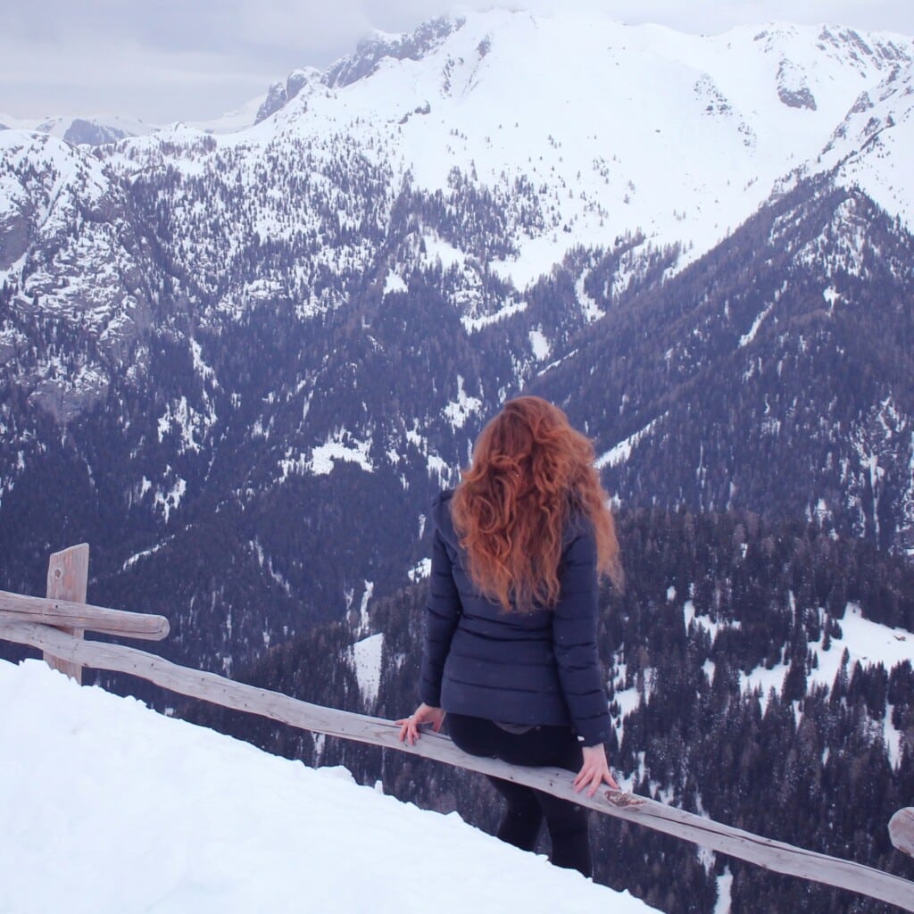 6 ways to embrace the cold weather, water signs! - redhead woman sitting on fence on mountain looking out over winter snowscape
