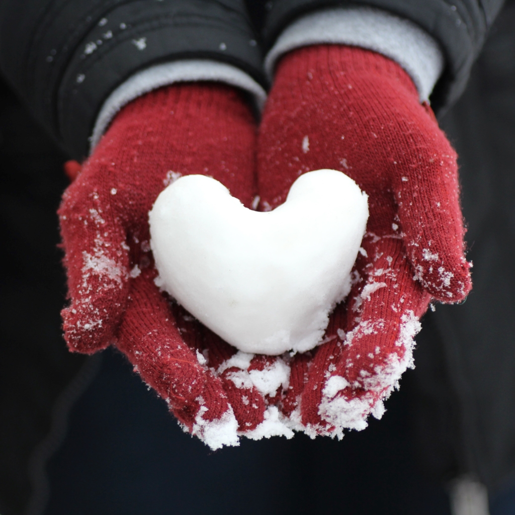 Plan an epic snowball fight - hands wearing red winter gloves and holding a snowball shaped as a heart