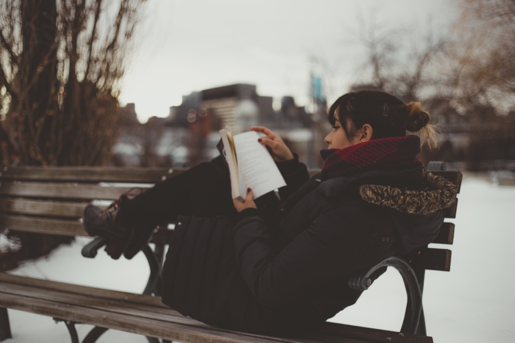 Aries - Thriller and Suspense - model curled up on outdoor park bench reading a book in winter landscape