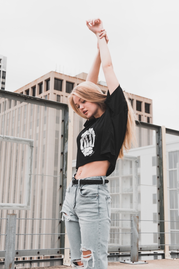 Young woman posing outside wearing ripped jeans and a skeleton hand crop top shirt