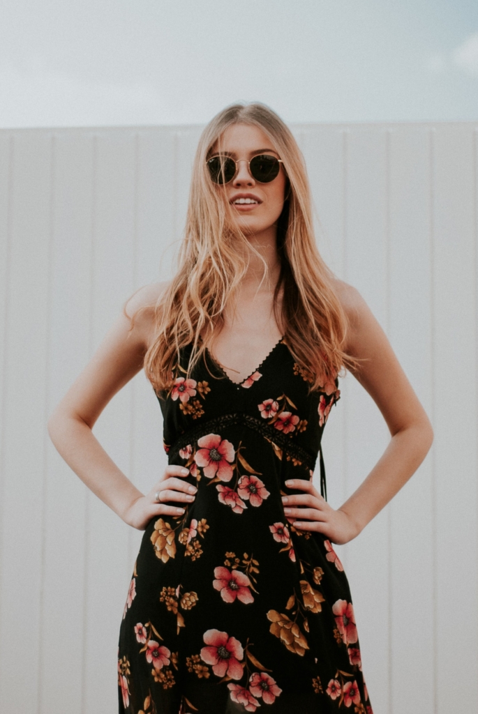 A feminine flair - model smiling with hands on hips wearing a black floral empire waist dress and sunglasses