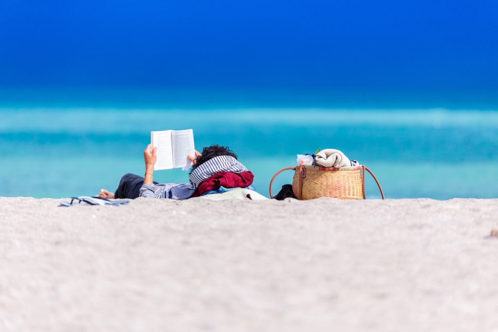 Leo - comedy - woman lying on towel on beach reading a book
