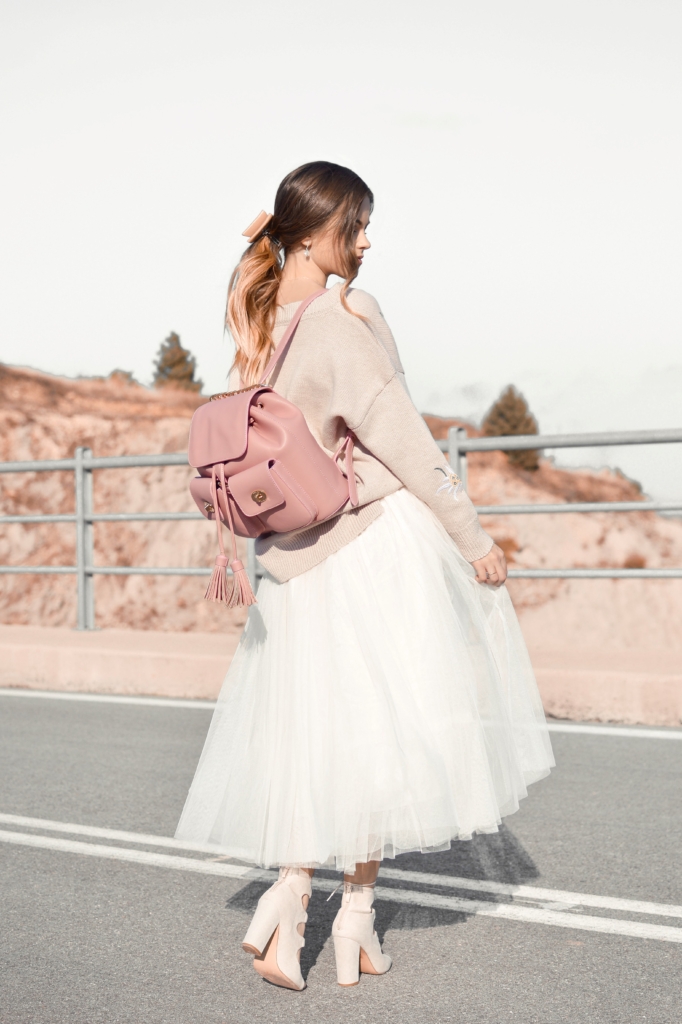 Barbiecore - model standing on road wearing a white ball gown and cream floral jacket and soft pink backpack