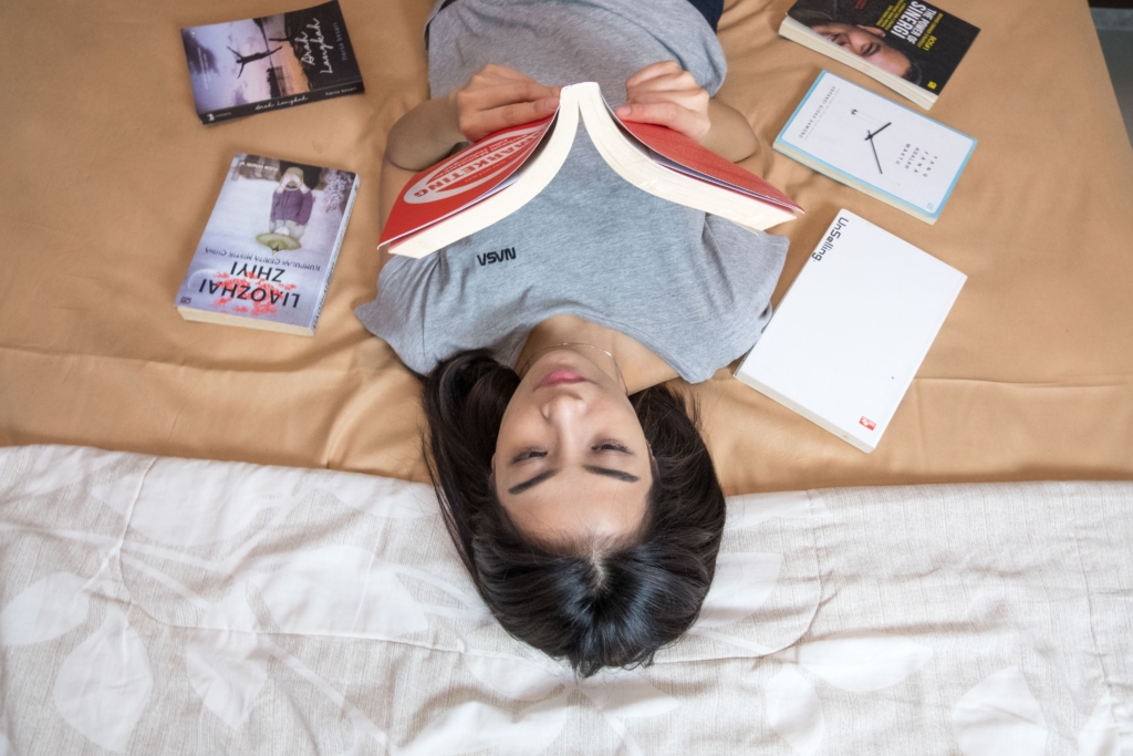 Virgo - science fiction - model lying on bed wearing a NASA shirt and reading a book with books on bed around her