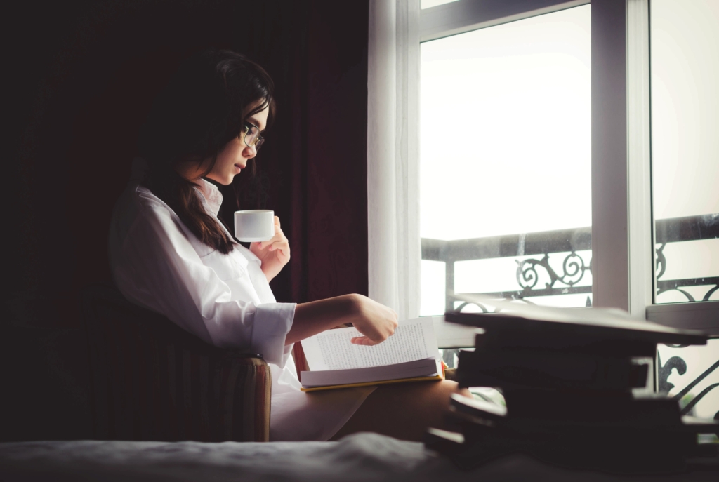 Virgo - science fiction - woman sitting in chair at window reading a book and drinking from hot mug