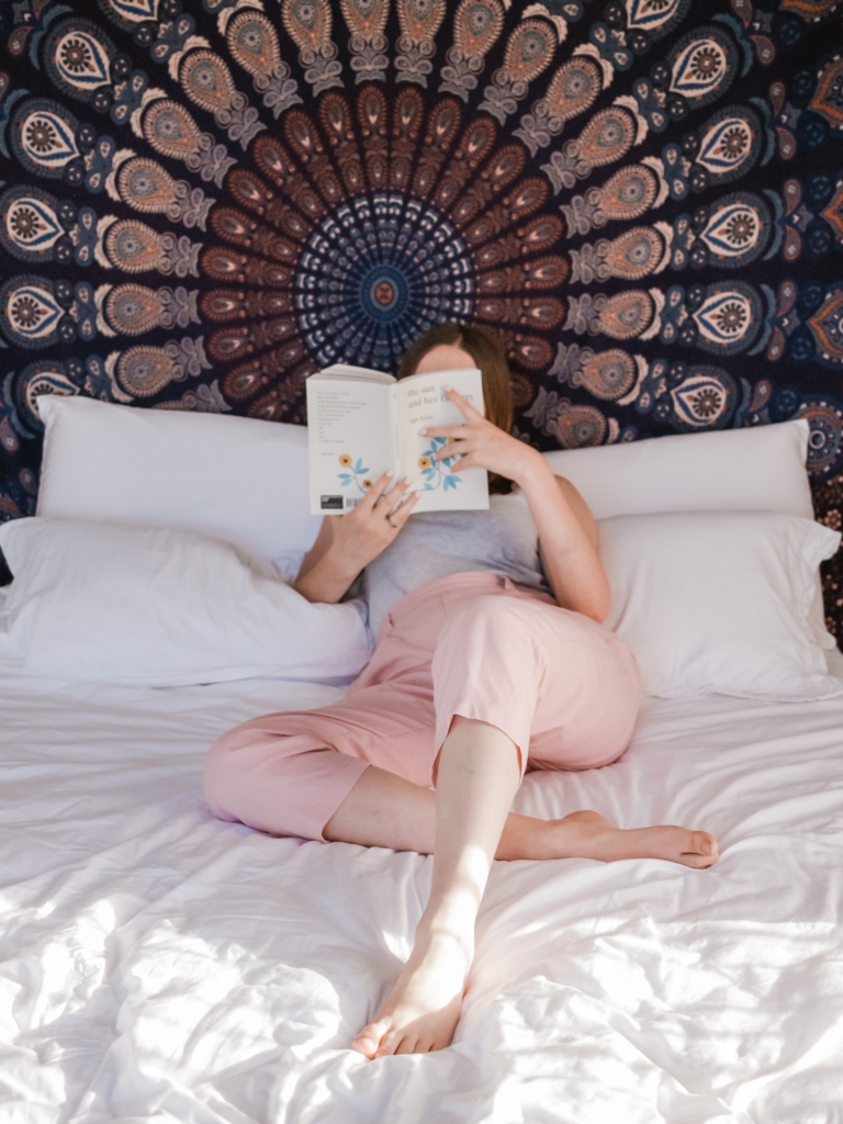 Sagittarius- philosophy- woman lying in bed reading a book and with a large mandala design covering wall
